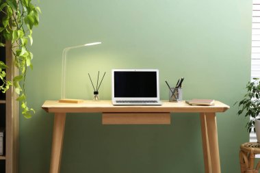 Home office. Comfortable workplace near light green wall. Desk with laptop and lamp in room
