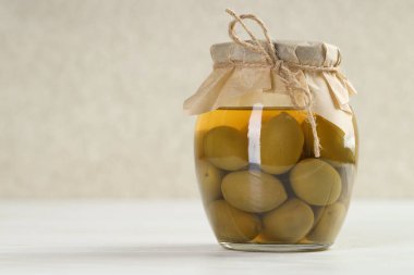 Beyaz masada cam kavanozda yeşil zeytin turşusu, yakın plan. Metin için boşluk