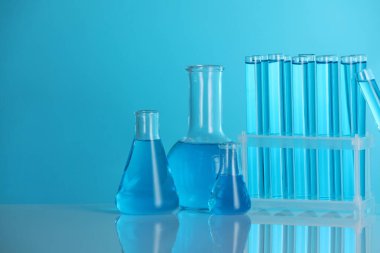 Aynanın yüzeyinde mavi arka planda sıvı bulunan laboratuvar camları. Metin için boşluk