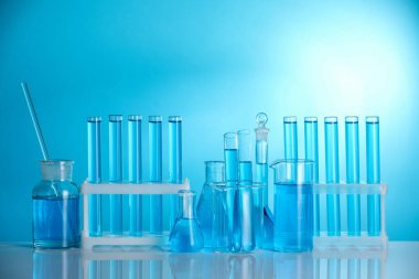 Aynanın yüzeyinde mavi arkaplana karşı sıvı bulunan laboratuvar camları.