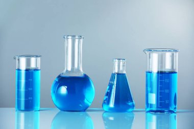 Aynanın yüzeyinde gri arka planda mavi sıvı bulunan laboratuvar camları