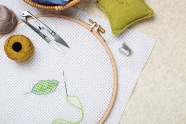 Embroidery and different sewing accessories on beige textured table, flat lay