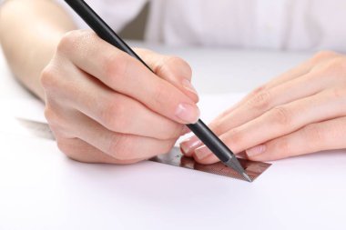Beyaz masada cetvel ve kalemle resim çizen kadın, yakın plan.
