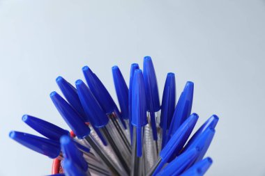 Many ballpoint pens in holder on light grey background, closeup