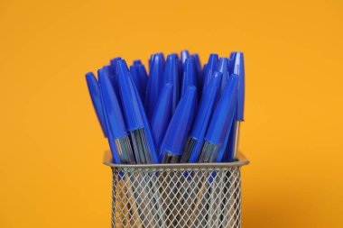 Many pens in holder on orange background, closeup