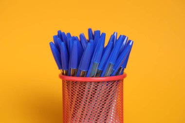 Many pens in holder on orange background, closeup