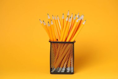 Many pencils in holder on orange background
