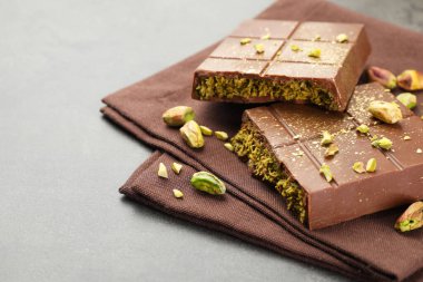 Pieces of tasty Dubai chocolate with pistachios and knafeh on grey table, closeup. Space for text