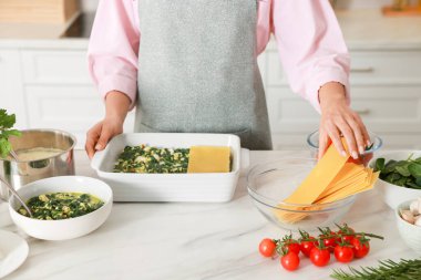 İçerideki mermer masada ıspanaklı lazanya yapan kadın, yakın plan.