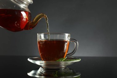 Koyu ayna masasında çaydanlıktan fincana taze demlenmiş çay dökülüyor.