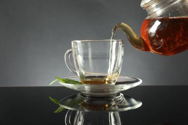 Koyu ayna masasında çaydanlıktan fincana taze demlenmiş çay dökülüyor.