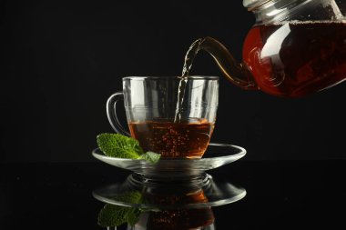 Koyu ayna masasında çaydanlıktan fincana taze demlenmiş çay dökülüyor.