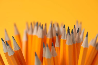 Many graphite pencils on orange background, closeup