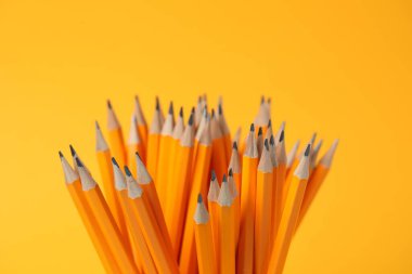 Many graphite pencils on orange background, closeup