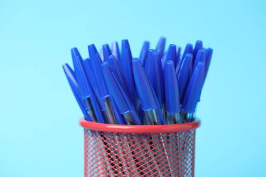 Many ballpoint pens in holder on light blue background, closeup