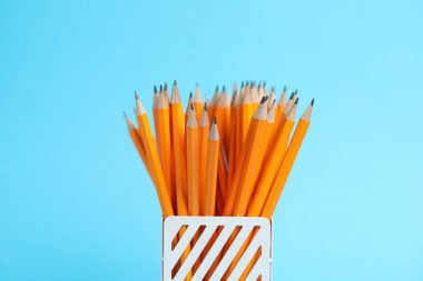 Many graphite pencils in holder on light blue background, closeup