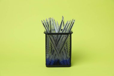 Many ballpoint pens in holder on green background