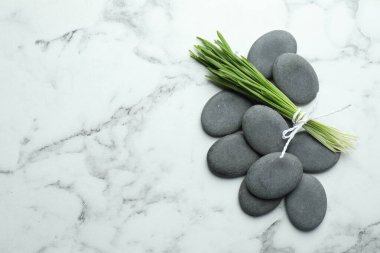 Spa stones and wheatgrass on white marble background, flat lay. Space for text