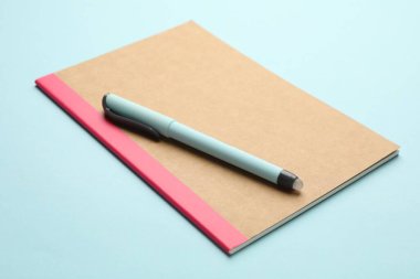 Copybook and pen on light blue background, closeup