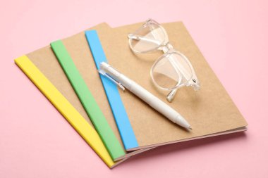 Different copybooks, pen and glasses on pink background, closeup