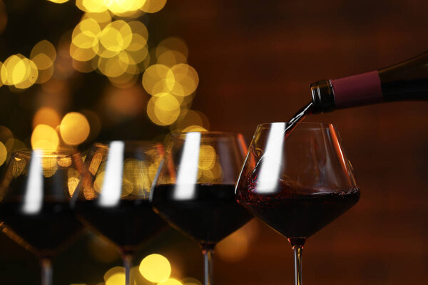 Выливать красное вино в бокал против размытых огней, крупным планом. Эффект Боке