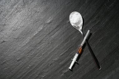 Drug addiction. Spoon with powder and syringe on dark textured table, flat lay. Space for text