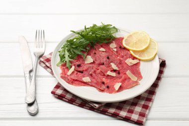 Fresh beef carpaccio with arugula, lemon and cheese on white wooden table, closeup