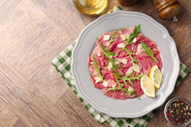 Fresh beef carpaccio with arugula, cheese and lemon on wooden table, flat lay. Space for text