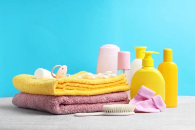 Bebek kozmetik ürünleri, çoraplar, emzik ve banyo aksesuarları açık mavi arka plana karşı gri desenli masa üzerinde