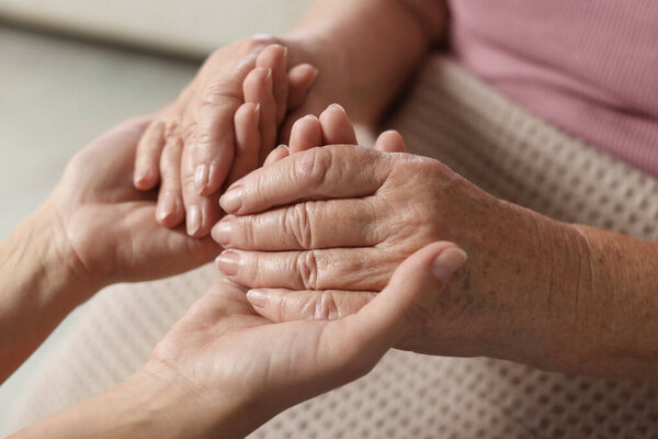 Caregiver supporting senior woman on light background, closeup. Elderly care