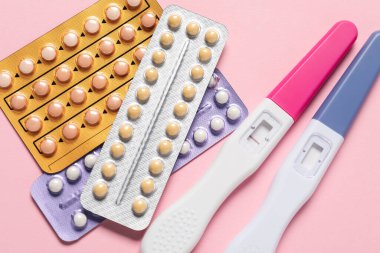 Blisters of oral contraceptive pills and pregnancy tests on pink background, flat lay