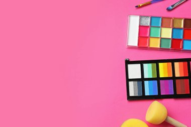 Bright face paints, brushes and sponges on pink background, flat lay. Space for text