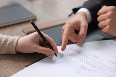 Belgeye işaret eden noter ve müşteri, kapalı oturulan ahşap masaya imza atıyor, yakın plan