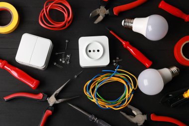 Different electrical tools on black wooden table, flat lay