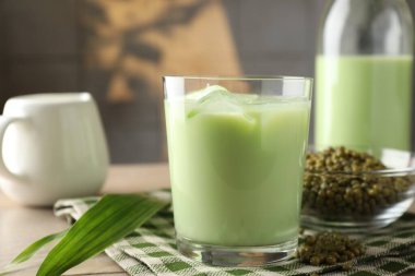 Fresh mung bean juice with ice in glass, milk, leaves and seeds on wooden table, closeup