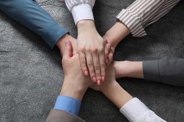 Business concept. Group of people stacking hands at grey textured table, top view