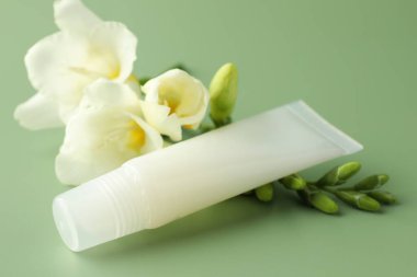 Açık yeşil arka planda dudak kremi ve frezya çiçekleri, yakın plan.