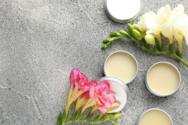 Nemlendirici dudak kremleri ve gri desenli masa üzerinde güzel çiçekler. Metin için boşluk