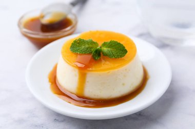 Beyaz mermer masada servis edilen karamel soslu lezzetli puding, yakın plan.
