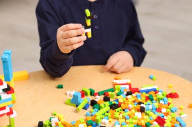 Hoş çocuk ahşap masada yapı taşlarıyla oynuyor, yakın plan.