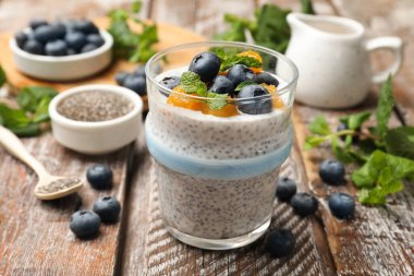 Delicious chia pudding with blueberries, peaches and mint in glass on wooden table, closeup