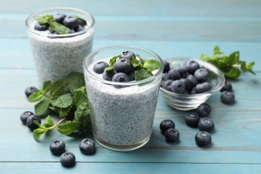 Delicious chia pudding with blueberries and mint in glasses on light blue wooden table, closeup