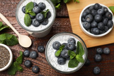 Delicious chia pudding with blueberries and mint in glasses on wooden table, flat lay