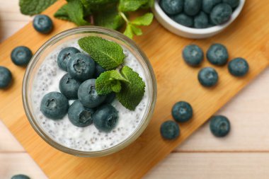 Delicious chia pudding with blueberries and mint in glass on wooden table, top view