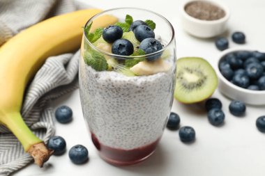 Delicious chia pudding with blueberries, kiwi, banana and mint in glass on light table, closeup