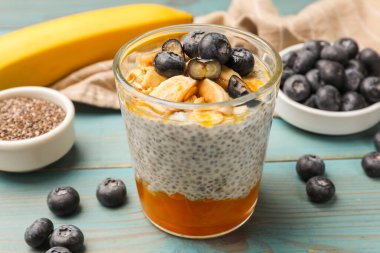 Delicious chia pudding with blueberries, banana and oatmeal in glass on light blue wooden table, closeup