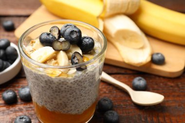 Delicious chia pudding with blueberries and banana in glass on wooden table, closeup