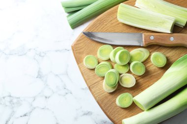 Chopped leeks, knife and board on white marble table, flat lay. Space for text