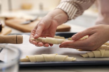 Kadın, masadaki yemek masasına çiğ kruvasan koyuyor, yakın plan.