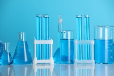 Aynanın yüzeyinde mavi arkaplana karşı sıvı bulunan laboratuvar camları.